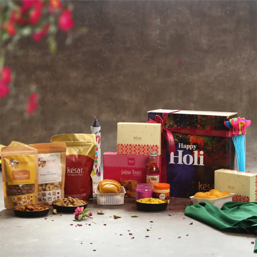 Lovely Holi Fiesta Gift Hamper featuring Kesar Gujiya, Mini Samosas, flavored nuts, colorful gulal, a color bomb, water balloons, and a greetings card in a vibrant decorative box.