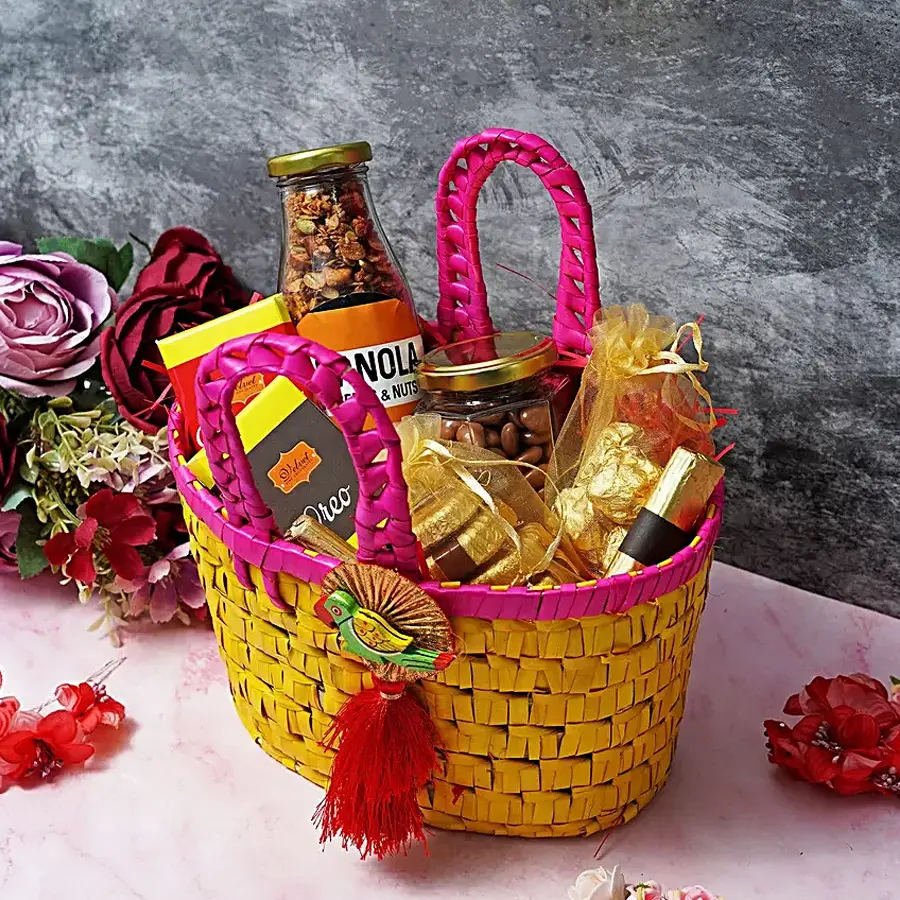 A beautifully arranged basket filled with assorted sweet treats including chocolate bars, almond florentines, chocolate-coated raisins, chocolate logs, chocolate almond rocks, and a granola bottle, perfect for Mother's Day.