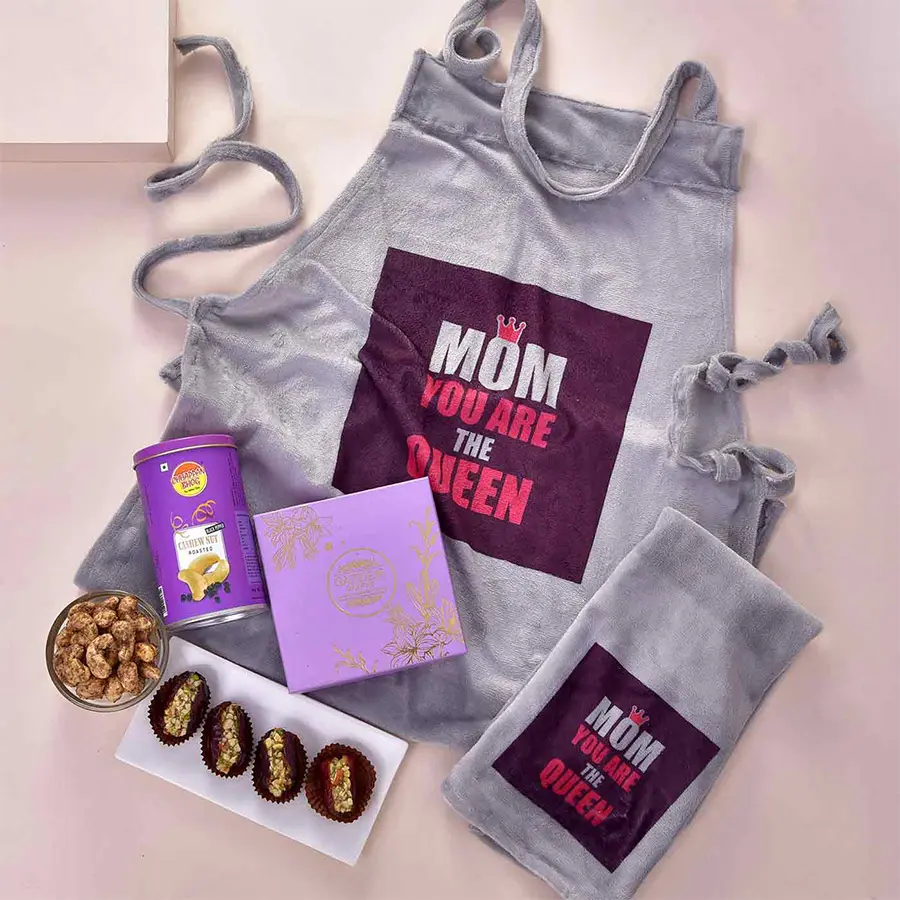 A beautifully arranged gift hamper for Mother's Day featuring a charming apron, hand cloth, Garden Bakery stuffed dates, and a can of premium roasted cashews.