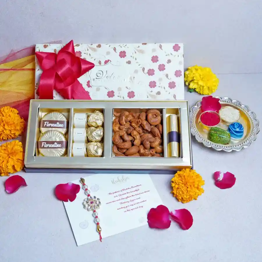 Nutty Chocolate Box featuring Chocolate Almond Florentines, assorted chocolates, Almond Rocks, Cajun Cashews, Orange Crisp Chocolate Log, a designer Rakhi, and a greetings card on a festive background.