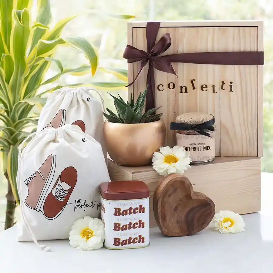 Caring Gift Hamper for Rakhi featuring personalized wooden heart bowl, copper planter with succulent, mixed nuts, choco chunk cookies, cotton drawstring shoe bag, Kundan rakhi, and reusable pinewood box.