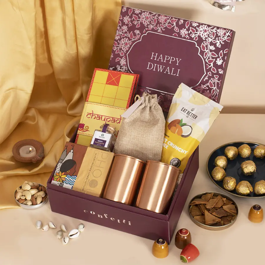 Red gift box filled with a Chaupad board, copper glass set, nut mix, saffron, and incense cones, decorated for Diwali celebration