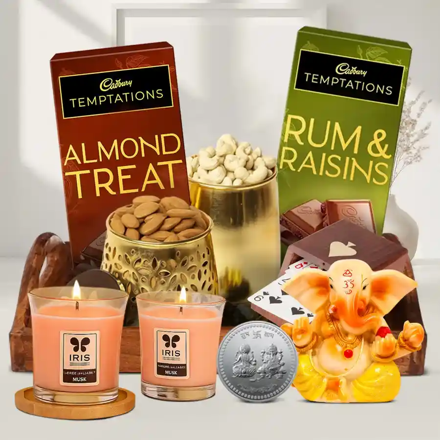 Tray of Diwali Surprises featuring copper jars of cashews and almonds, Iris scented candles, Vignesh Ganesh figurine, almond delights, rum raisins, playing cards, and a silver Ganesh Lakshmi coin on a designer wooden tray.