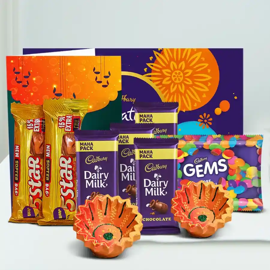 A beautifully arranged Diwali gift box featuring Cadbury chocolates, handcrafted clay diyas, and a Happy Diwali card, surrounded by colorful decorations.