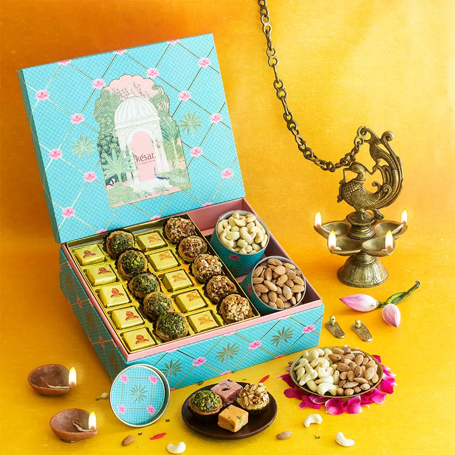 Delectable Diwali Treat Box featuring assorted bites, pista tarts, almond tarts, and packs of roasted cashews and almonds in a pink and blue Jharokha box