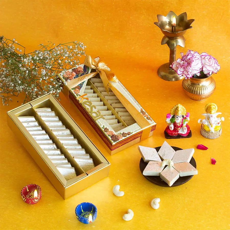 Ganesh Laxmi idol with a box of Kaju Katli, two diyas, and a Diwali greeting card arranged together.