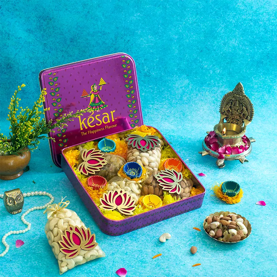 Exquisite Nut and Diya Ensemble in a Kesar Pink Diwali Special tin box with a vibrant Lotus Potli, featuring cashews, almonds, pistachios, raisins, and six colorful diyas.
