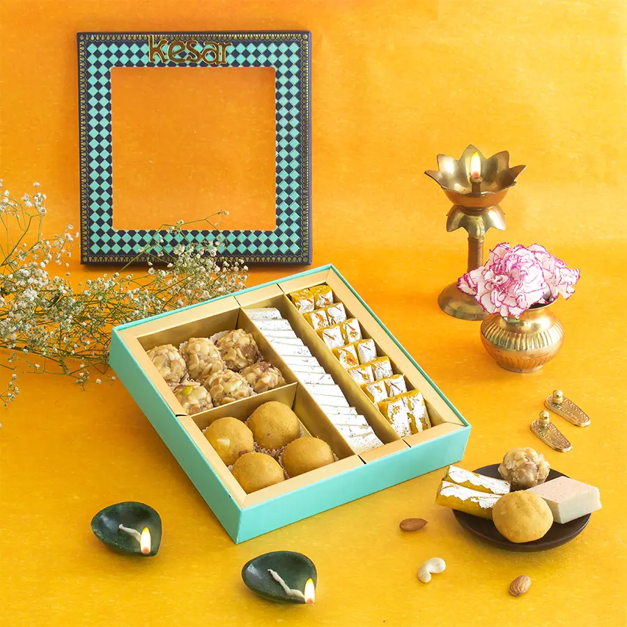 Assorted sweets including Dryfruit Laddoo, Besan Laddoo, Kaju Katli, and Kaju Kesar Roll in a blue window box