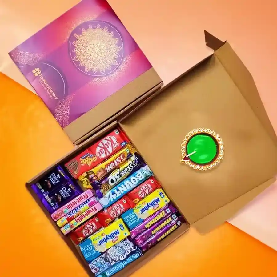 Festive hamper featuring an assortment of chocolates including KitKat, Cadbury, and Bounty, alongside a decorative diya, set against a colorful background for Diwali celebrations.