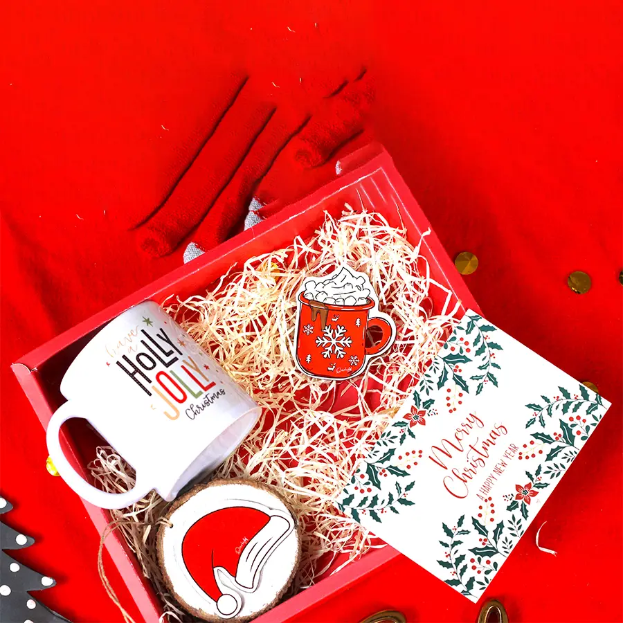Festive Fusion Gift Set featuring a quirky fridge magnet, rustic sliced log hanging, Christmas mug, and a beautifully crafted postcard arranged on a holiday-themed background.