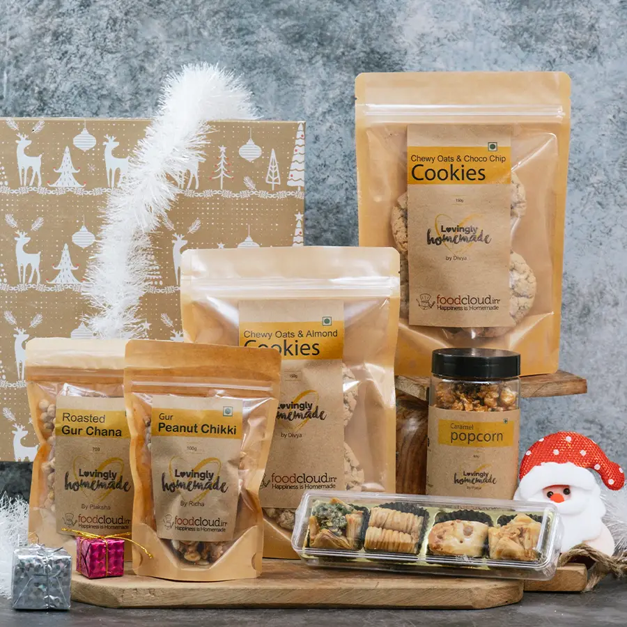 Crunchy Christmas Munchies Hamper filled with Oats & Chocochip Cookies, Almond Cookies, Caramel Popcorn, Gur Chikki, Roasted Chana, and Baklava pieces, surrounded by festive decorations.