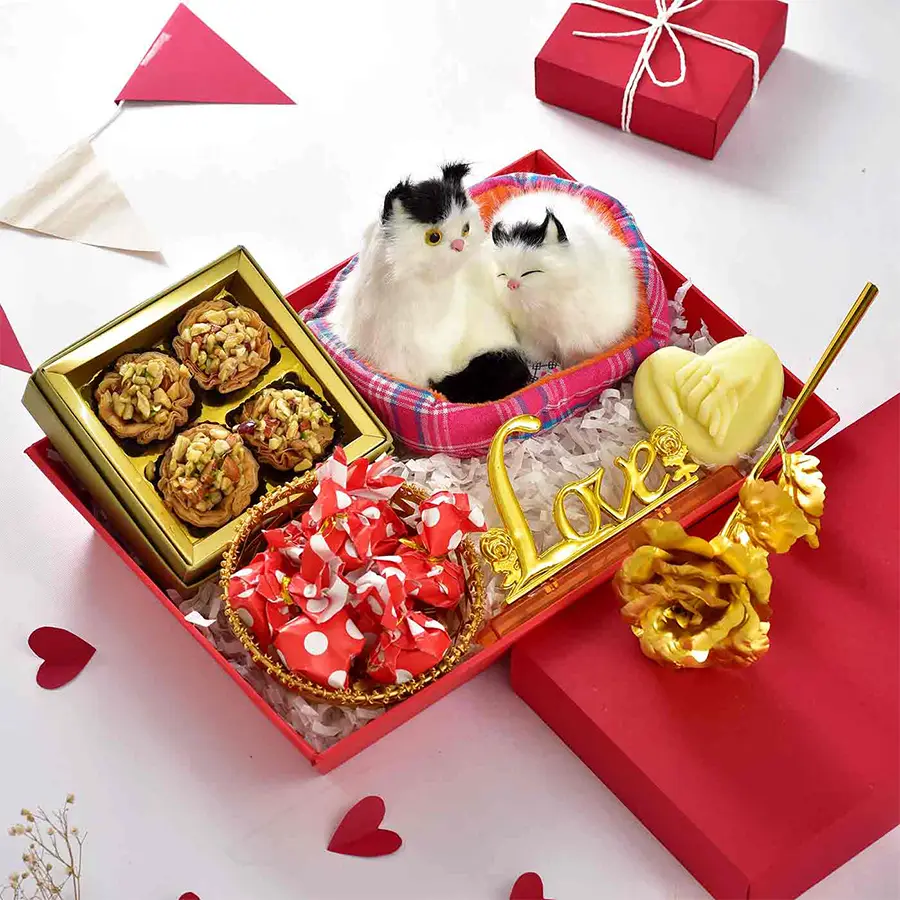 A vibrant red tray filled with an adorable cat couple showpiece, a stunning golden rose in a sleek stand, 4 tart baklawa, and 8 rich chocolates, all presented in a golden metal basket.