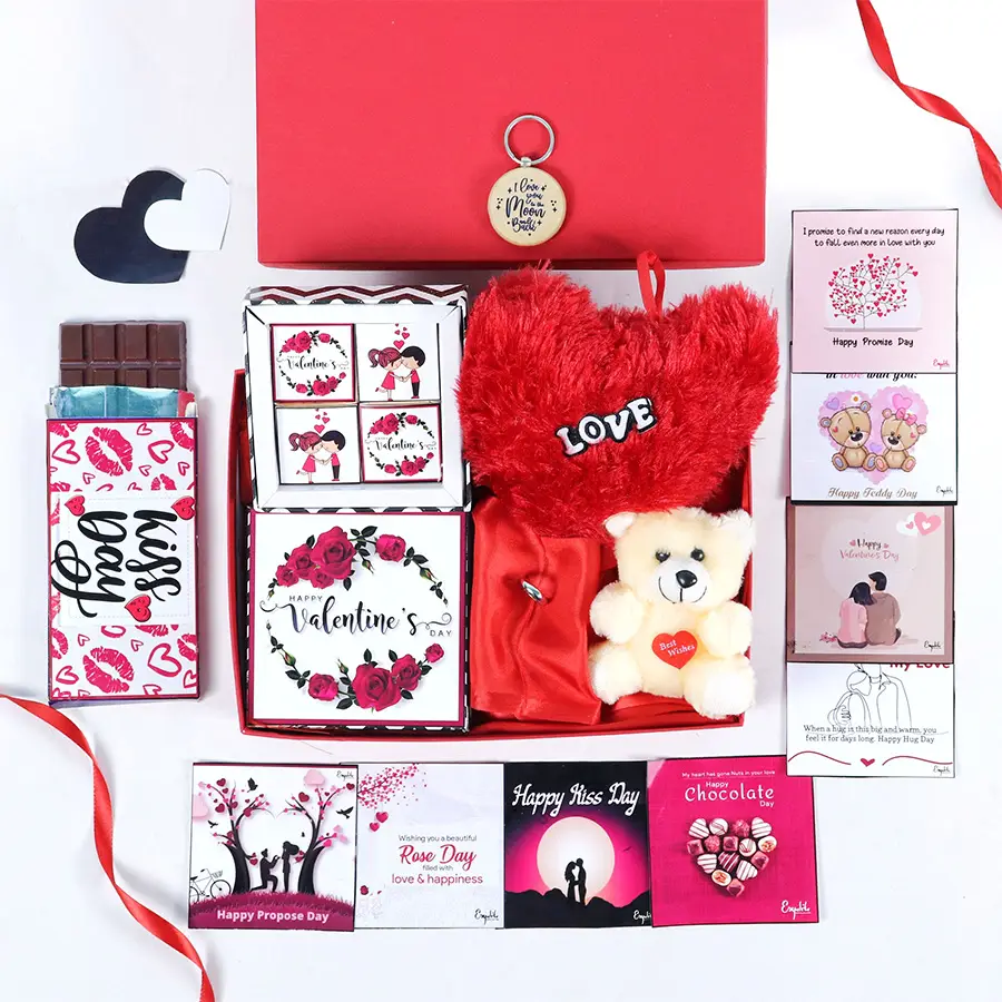 Valentine's Day hamper featuring red box, assorted chocolates, wooden keyring, heart-shaped pillow, teddy bear, silver ring, chocolate bar, and greeting cards.