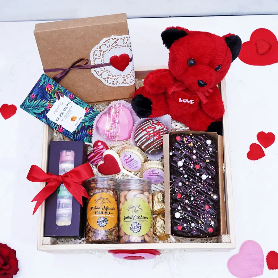 Gift box filled with assorted chocolates, teddy bear, and sweet treats including dark chocolate, chocolate pizza, hazelnut tea cake, heart-shaped chocolates, almond Florentines, chocolate lollipops, chocolate almond rocks, Italian trail mix, salted cashews, and macarons.
