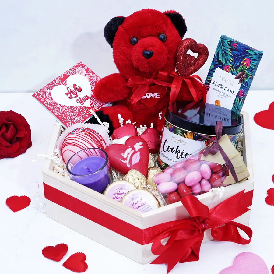 Valentines Chocolaty Indulgence Hamper featuring a cuddly teddy, cookies, a scented candle, Dark Belgian chocolate with candied orange, almond florentines, heart-shaped treats, a hot chocolate bomb, and a bottle of dragees.
