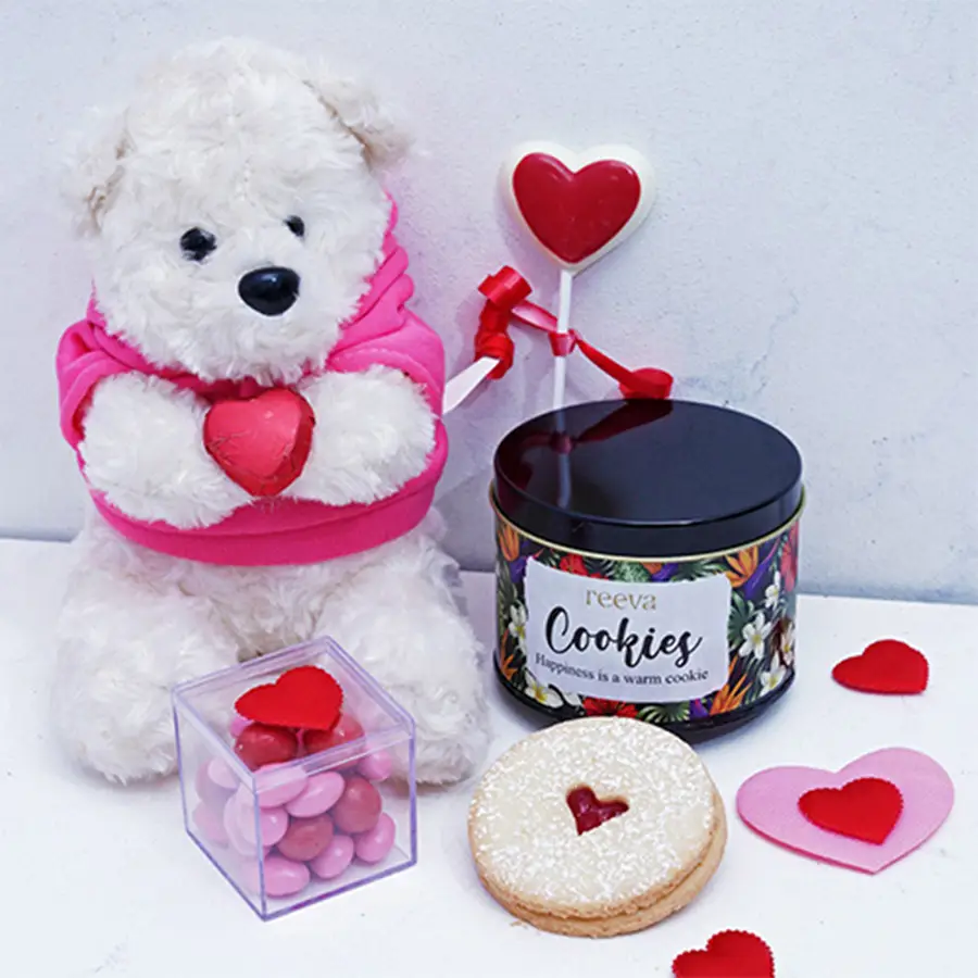 Blissful Valentines Day Treats Assortment featuring Jammie Dodgers Cookies, Almond Rose and Cranberry Dragees, a heart-shaped chocolate lollipop, and a cuddly teddy bear in a charming tin.