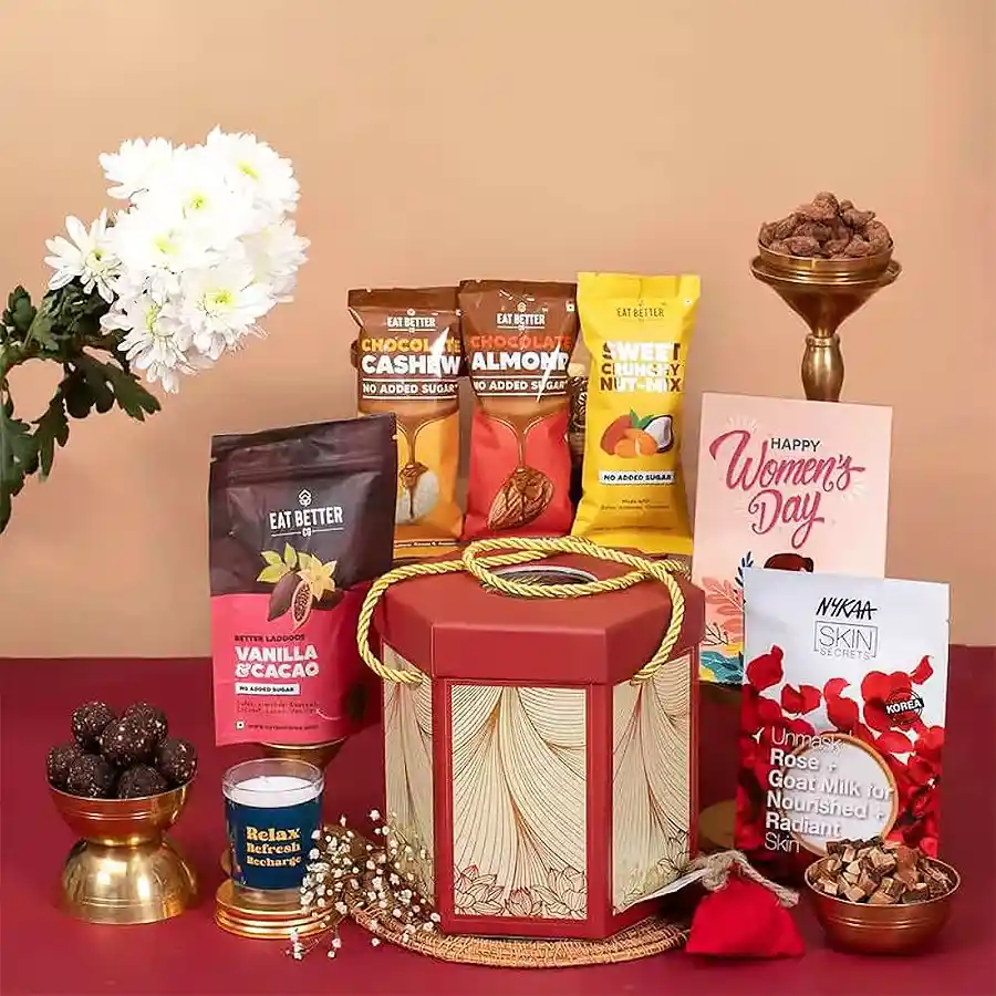Women's Day Indulgence Gift Box featuring Vanilla Chocolate Laddoos, Chocolate Almonds and Cashews, Nut Mix, a scented candle, Nykaa sheet mask, Seed Ball, and a greeting card.