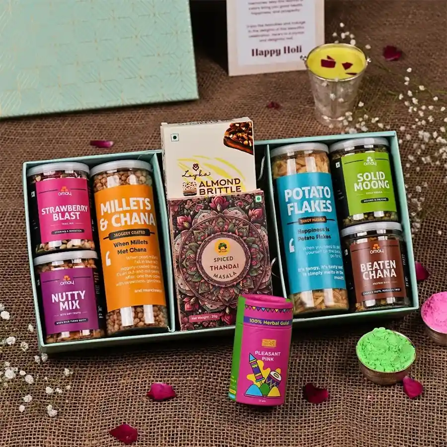 Delectable Festive Treats Galore gift box featuring assorted snacks including jaggery-coated millets, potato flakes, beaten chana, strawberry blast trail mix, nutty mix, almond brittle, instant thandai, and herbal gulaal, presented in a gold-foiled box with a personalized Holi greeting card.