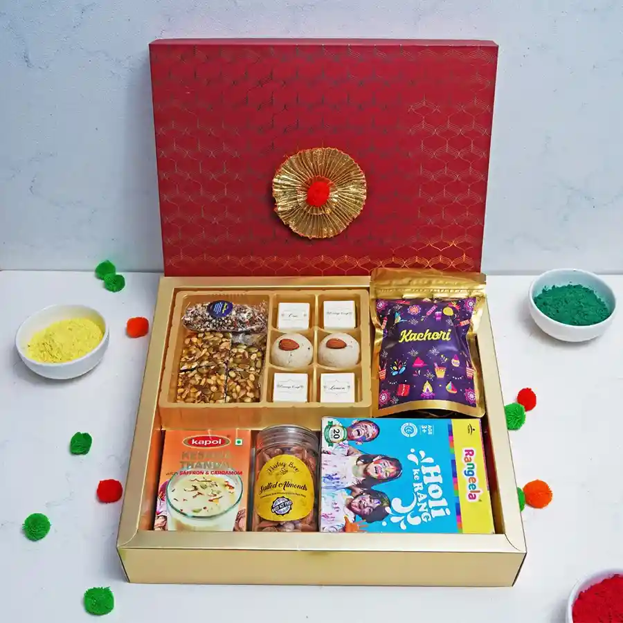 Festive Treats Box featuring Almond Fingers, Seeds Squares, assorted chocolates, Nankhatai, Kachori, Kesarai Thandai, salted almonds, and Holi colors.
