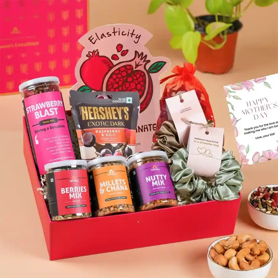 A beautifully arranged gift box featuring gourmet snacks, silk scrunchies, potpourri, a face mask, and a greeting card, all presented in a stunning gold package for Mother's Day.
