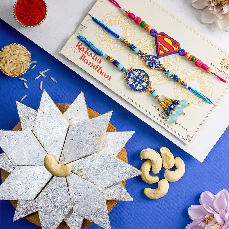 Trendy Family Rakhi Set featuring Kundan Bhaiya Bhabhi Rakhi, Superman Rakhi, 250g Kaju Katli, Roli, Tika, Chawal, and a heartfelt message card