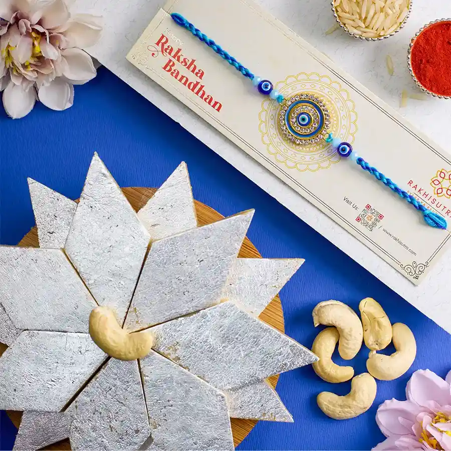 Stylish Evil Eye Rakhi and Kaju Katli combo with Roli, Tika, and Chawal on a decorative background.