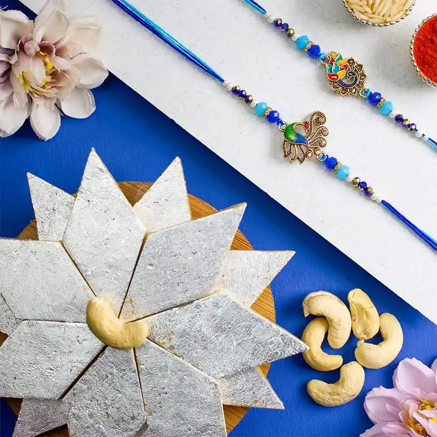 Kundan Rakhi set with two peacock-themed rakhis, Kaju Katli, Roli, Tika, Chawal, and a message card on a decorative background