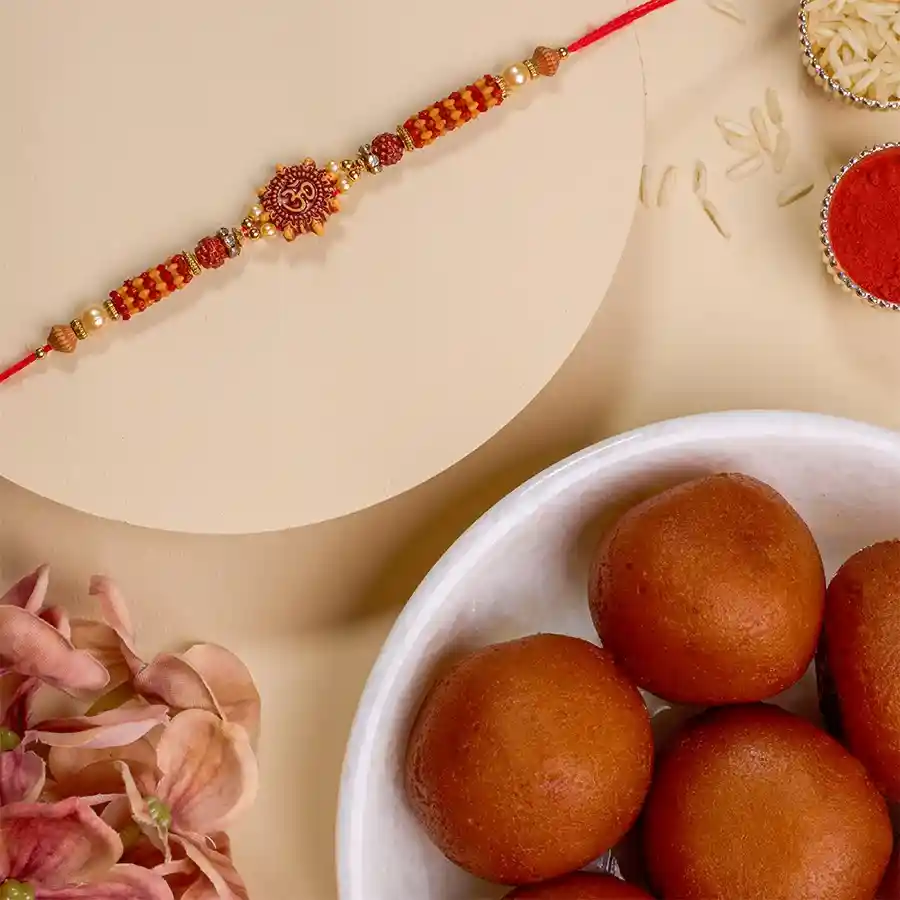 Blissful OM Rakhi with Gulab Jamun, Roli Tika, and Chawal on a decorative background