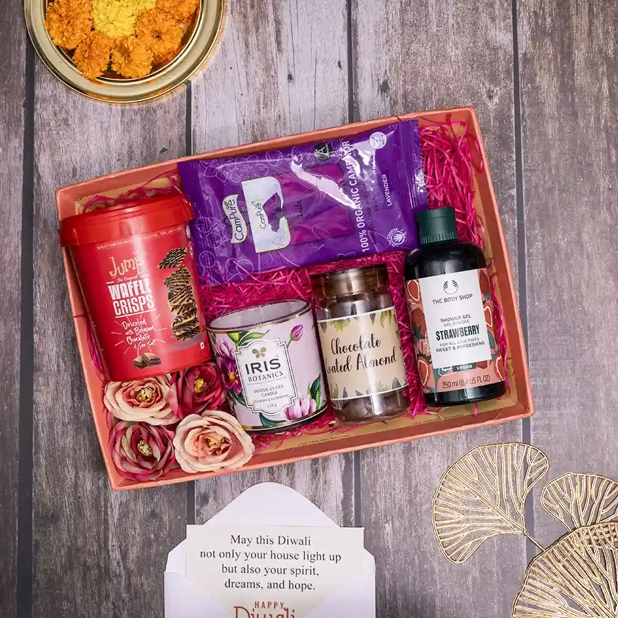 A beautifully arranged hamper filled with gourmet treats including waffle crisps, chocolate-coated almonds, shower gel, room freshener, and a votive candle, all in a reusable basket.